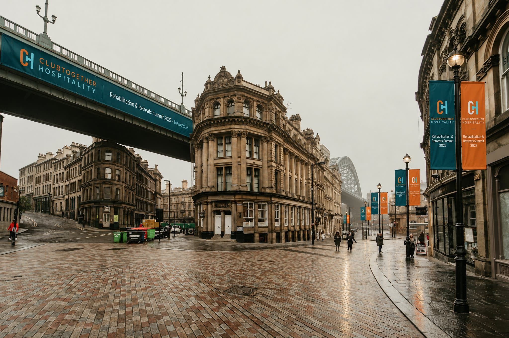 Summit banners on the lamp posts and a bridge above a Victorian street corner in Newcastle, with the Tyne Bridge in the mist