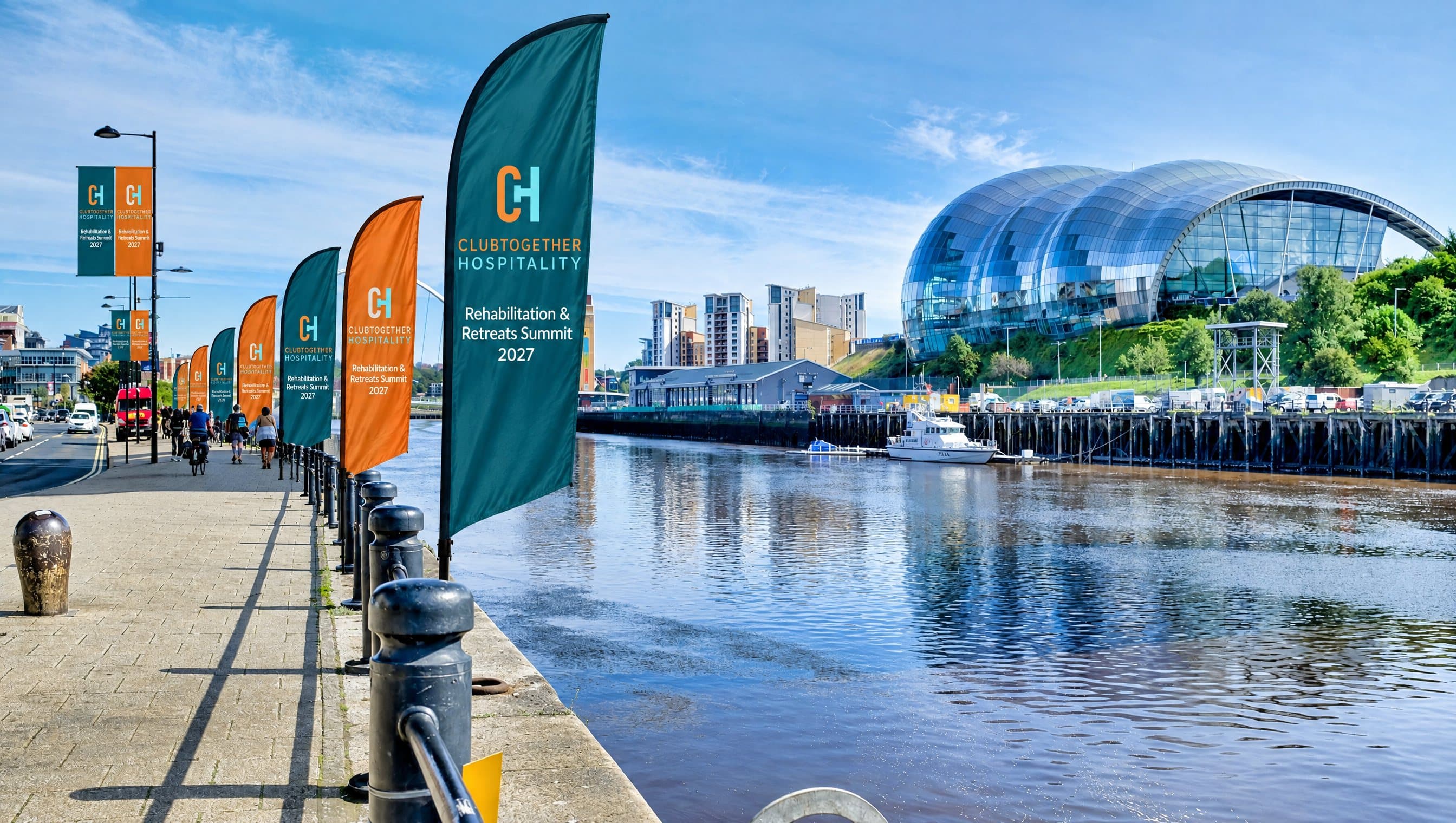 Summit flags lining the riverside promenade in summer sunshine, with the Sage across the river