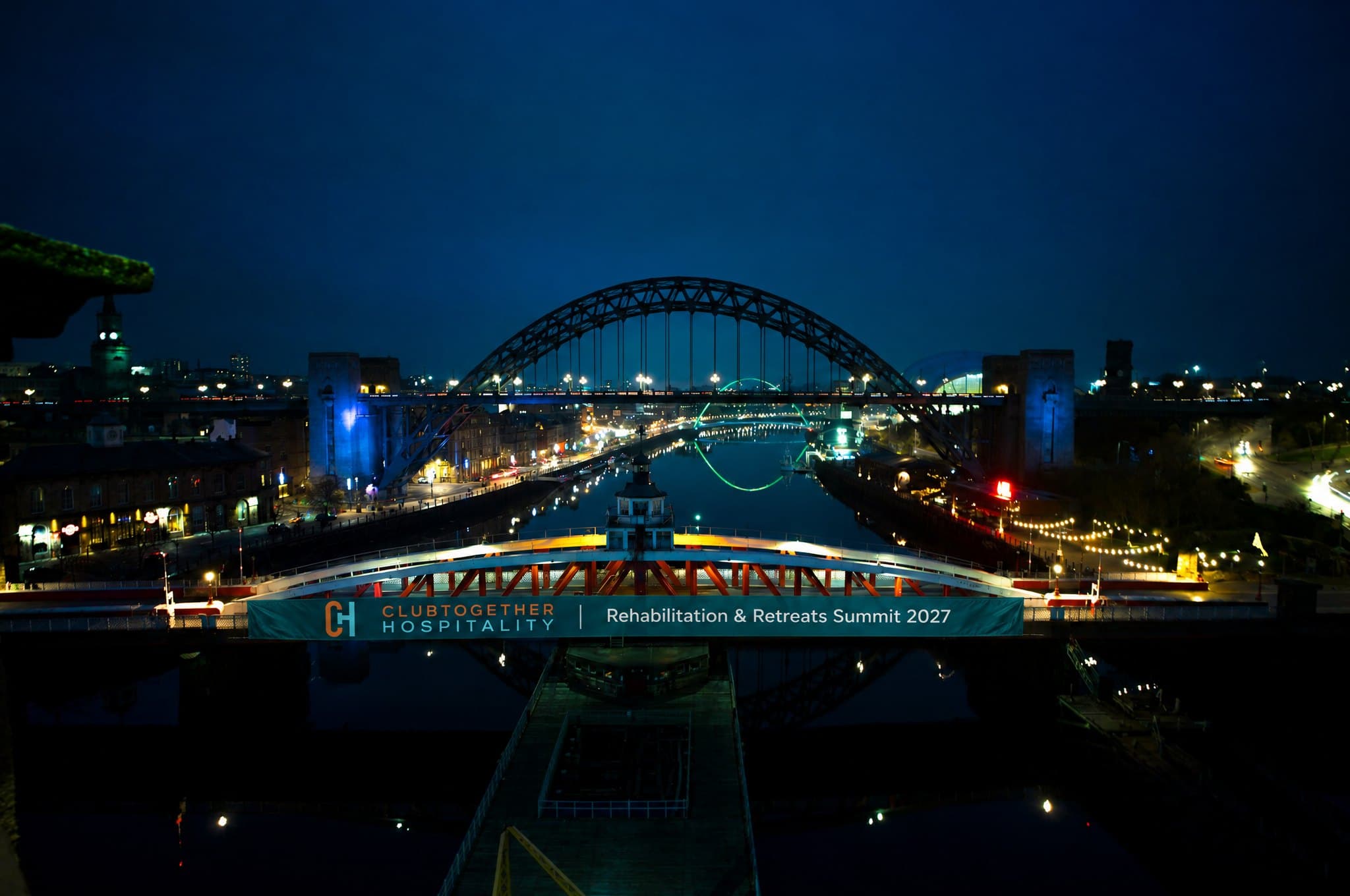 A summit banner on the Swing Bridge at night, with the Tyne Bridge lit up behind