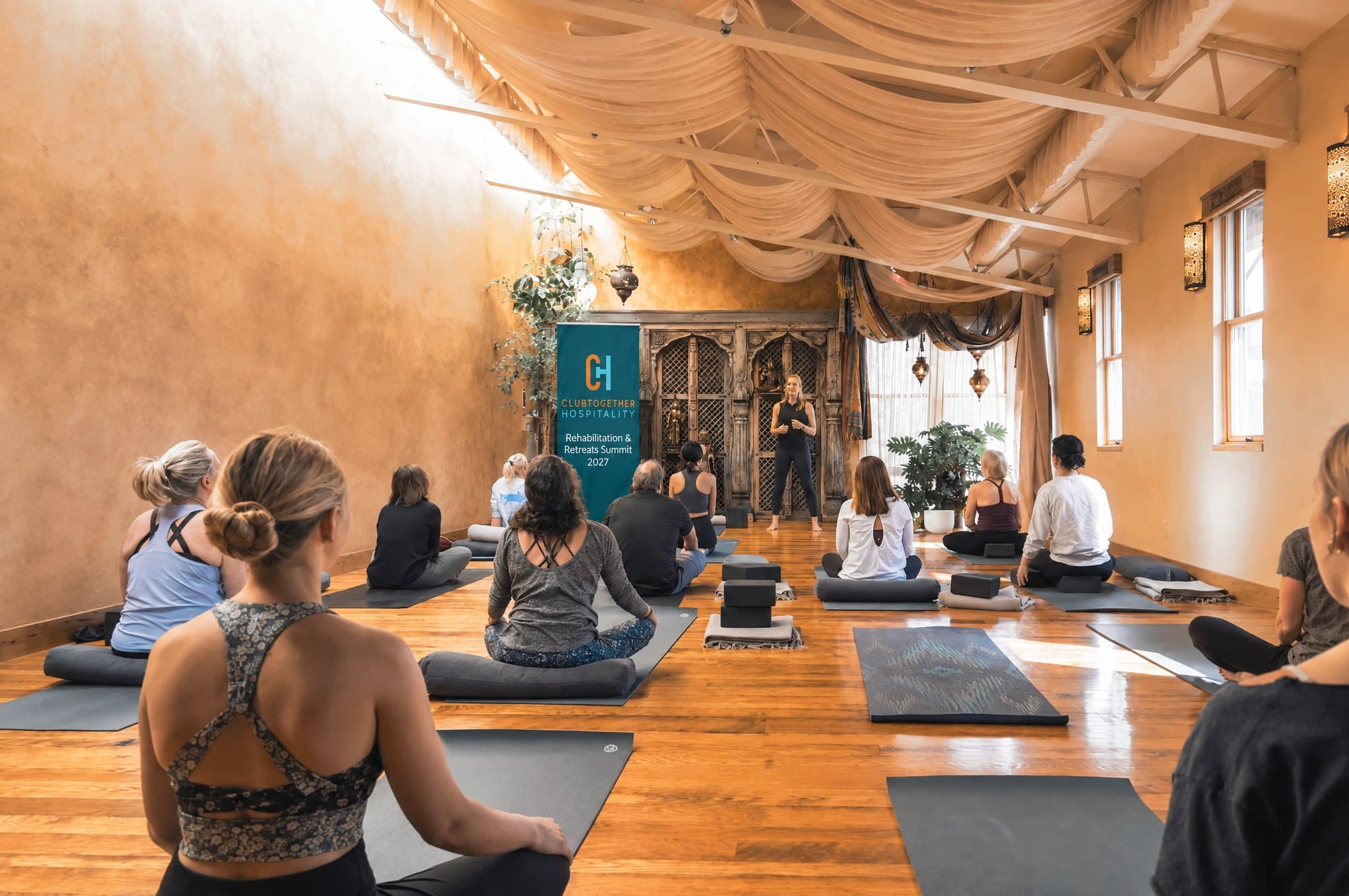 A gentle seated group session in a warm, sunlit studio, with a summit banner at the front